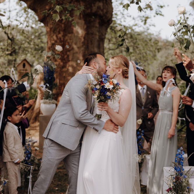 In der Hochzeitslocation Landgut Stober fand eine freie trauung direkt am See unter der großen Eiche statt und das Hochzeitspaar ließ sich am Ende des Spaliers feiern und sie küssten sich. Die Gäste hielten Blumen und ich bin extra aus Berlin angereist und begleitete die zwei professionell als Hochzeitsfotografin.